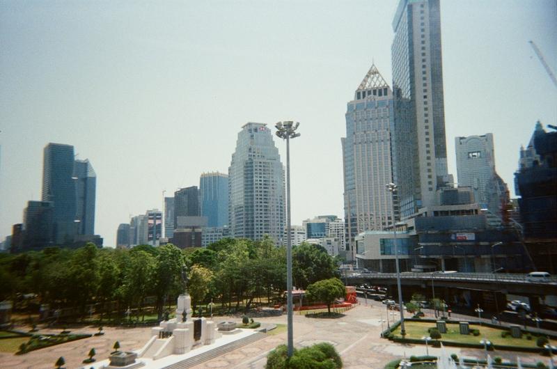 the corner of a park with some tall buildings in the background