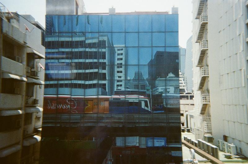 a BTS Sky Train reflected on the windows of a building as it passes by