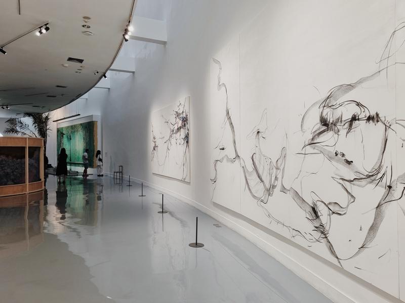 visitors standing among giant artworks hanging along the curved walls of the gallery: abstract charcoal paintings by Xiyao Wang