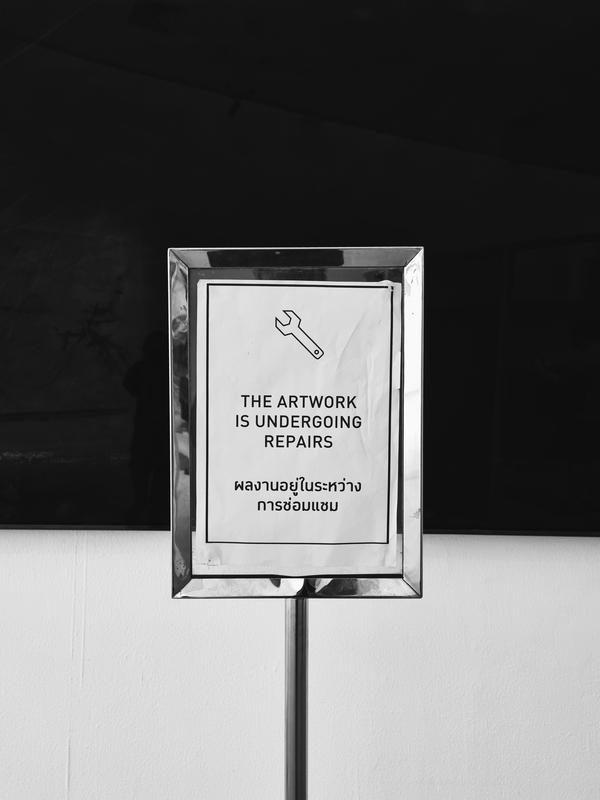 a sign in front of a powered-off screen that says 'The artwork is undergoing repairs'